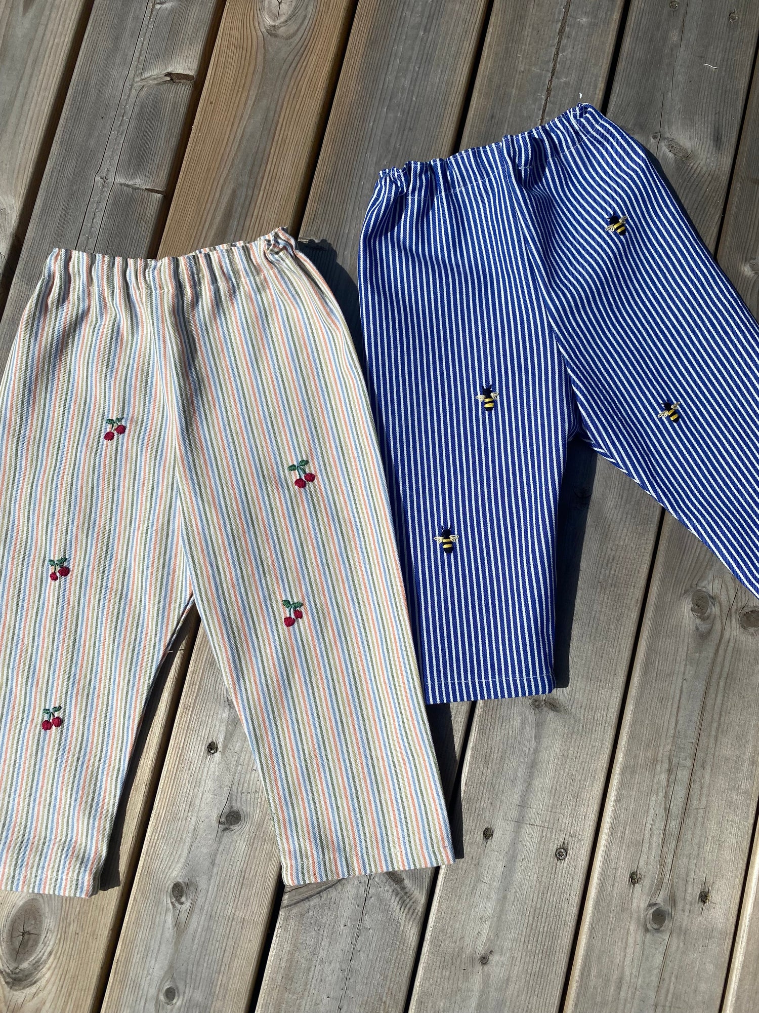 Billede af to par hjemmesyede bukser med håndbroderede bier og kirsebær